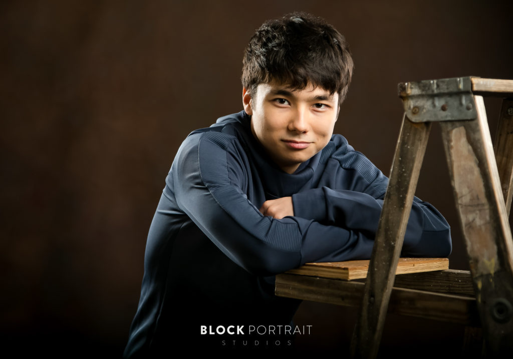 Picture of senior boy leaning on a ladder in Saint Paul studio by Block Portrait Studios