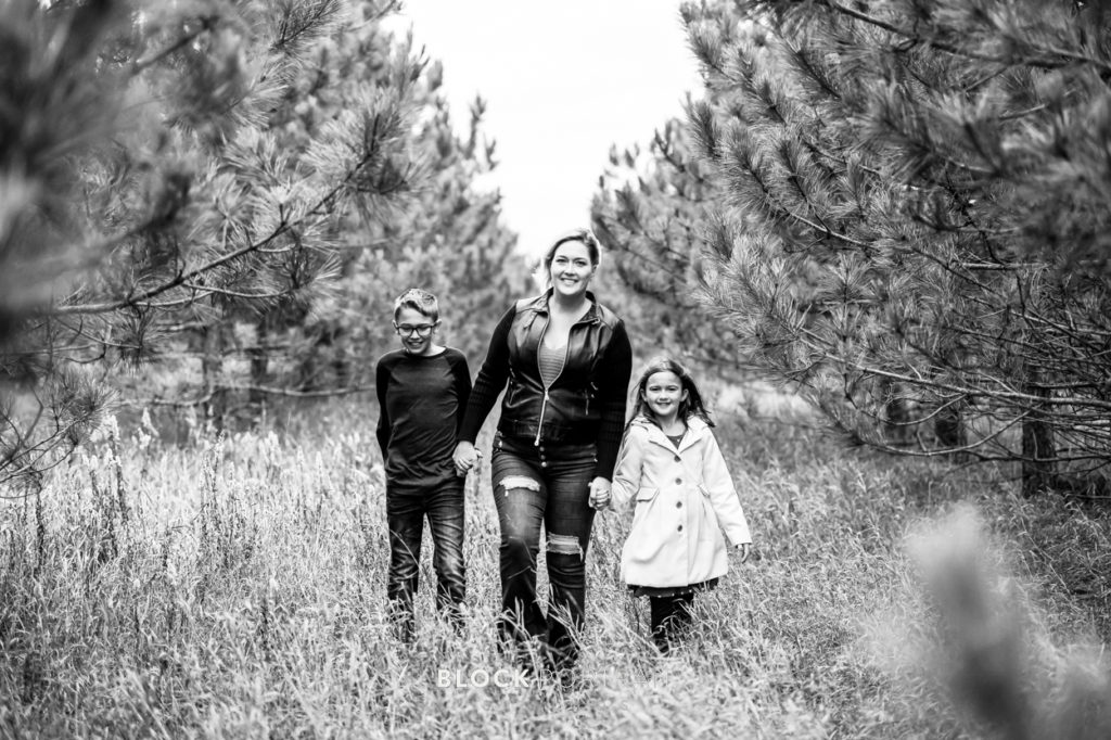 Black and white family portrait of a family walking through a field with trees surrounding them, taken by Saint Paul family portrait photographer Block Portrait Studios.