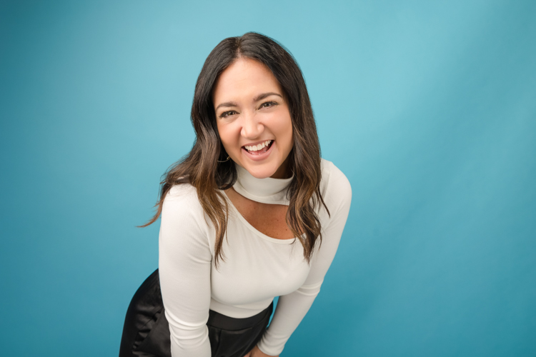 Marketing specialist smiling for branding photos in front of blue backdrop. Photographed at Block Portrait Studios
