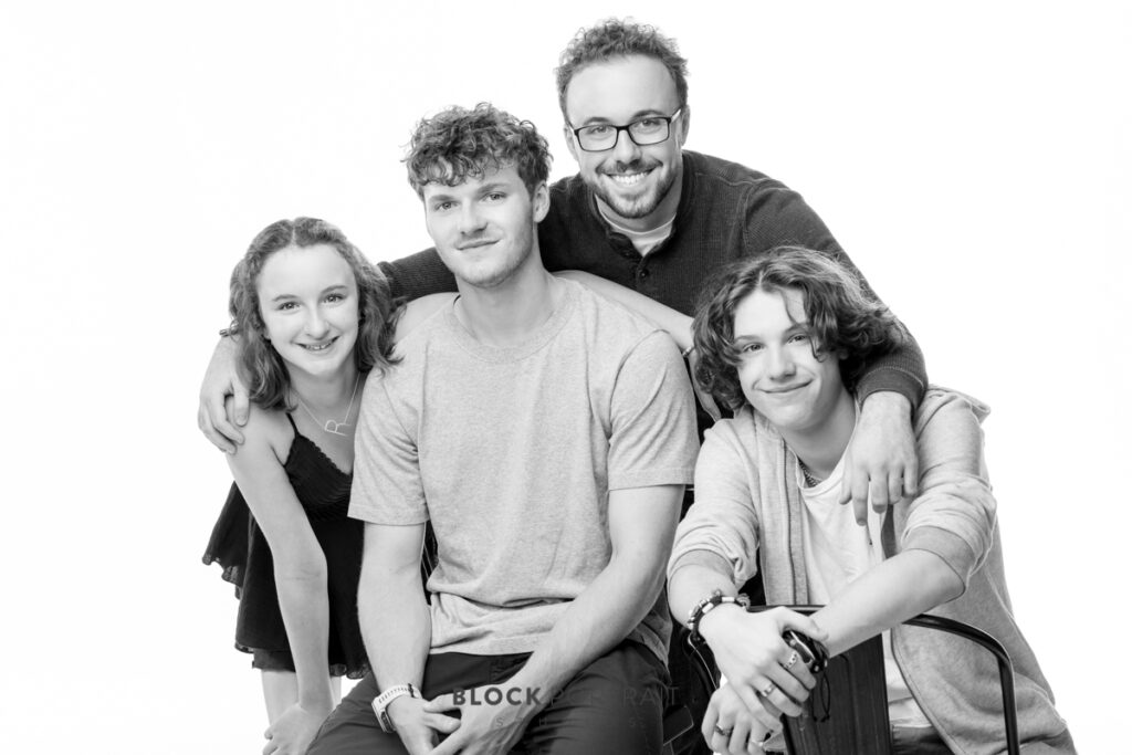 Black and white photo of four siblings with arms around each other smiling at the camera.